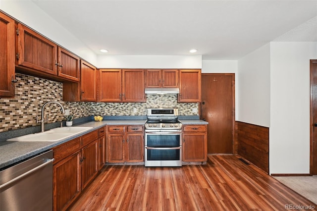 9125 Lowell Ct, Westminster, CO 80031 - kitchen with appliances with stainless steel finishes, under cabinet range hood, wood finished floors, backsplash, and brown cabinetry