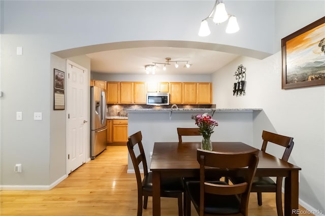 dining room with arched walkways, baseboards, and light wood-style flooring