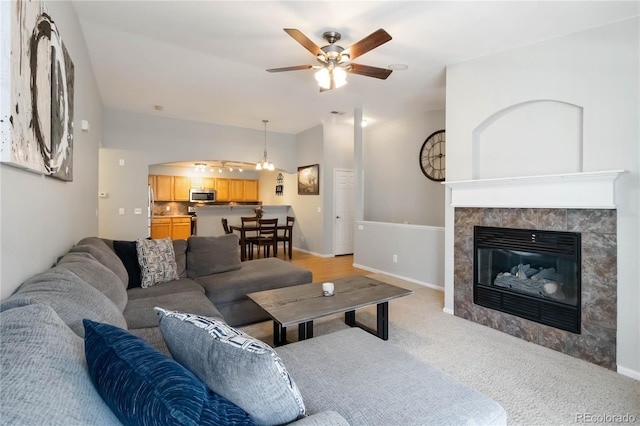 living room featuring baseboards, light colored carpet, arched walkways, a tiled fireplace, and a ceiling fan