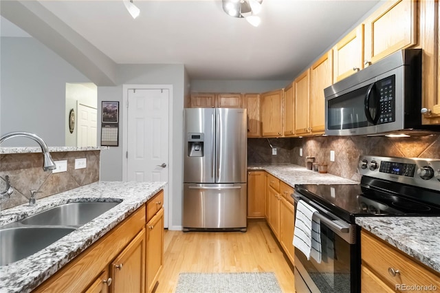 kitchen featuring light stone countertops, appliances with stainless steel finishes, a sink, light wood finished floors, and tasteful backsplash