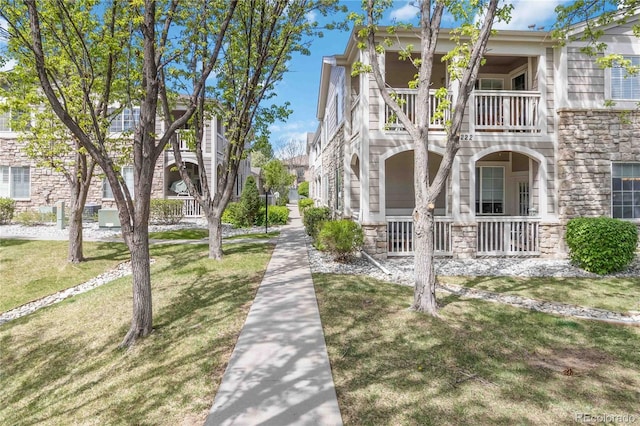 view of side of home featuring a balcony, covered porch, a yard, and stone siding