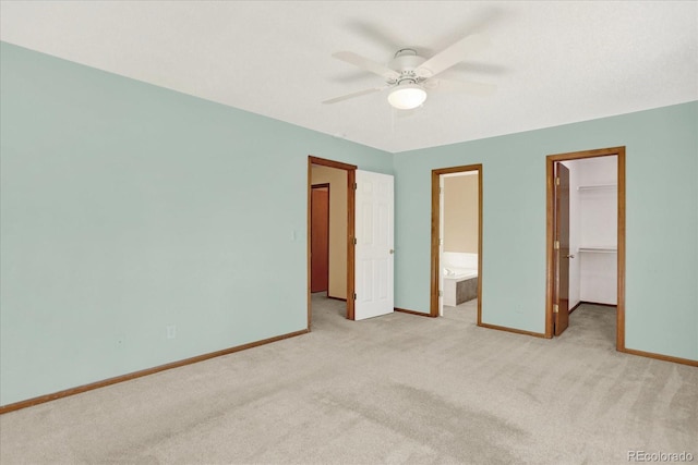 unfurnished bedroom with ensuite bath, a spacious closet, light carpet, a closet, and ceiling fan