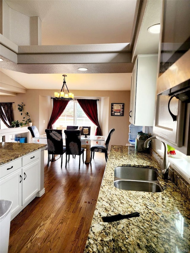 kitchen featuring dark wood-type flooring, light stone counters, a sink, and white cabinetry