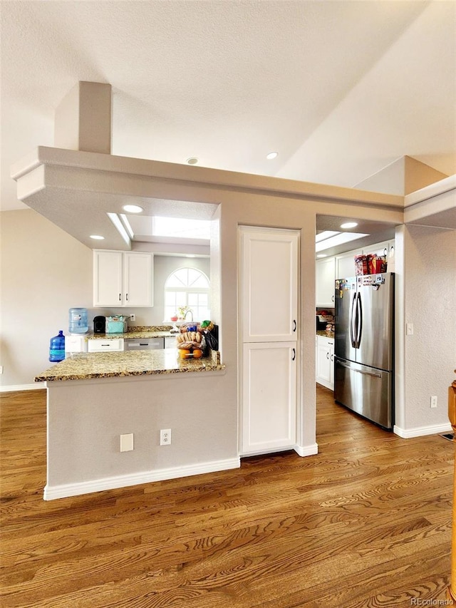 kitchen featuring white cabinets, freestanding refrigerator, wood finished floors, and light stone counters