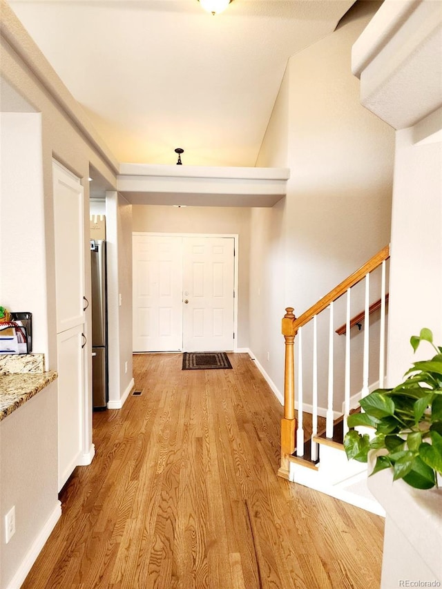 entrance foyer with light wood finished floors, baseboards, and stairway