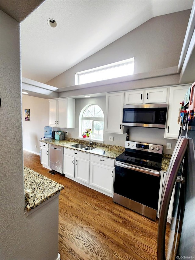 kitchen featuring white cabinets, a sink, wood finished floors, vaulted ceiling, and stainless steel appliances
