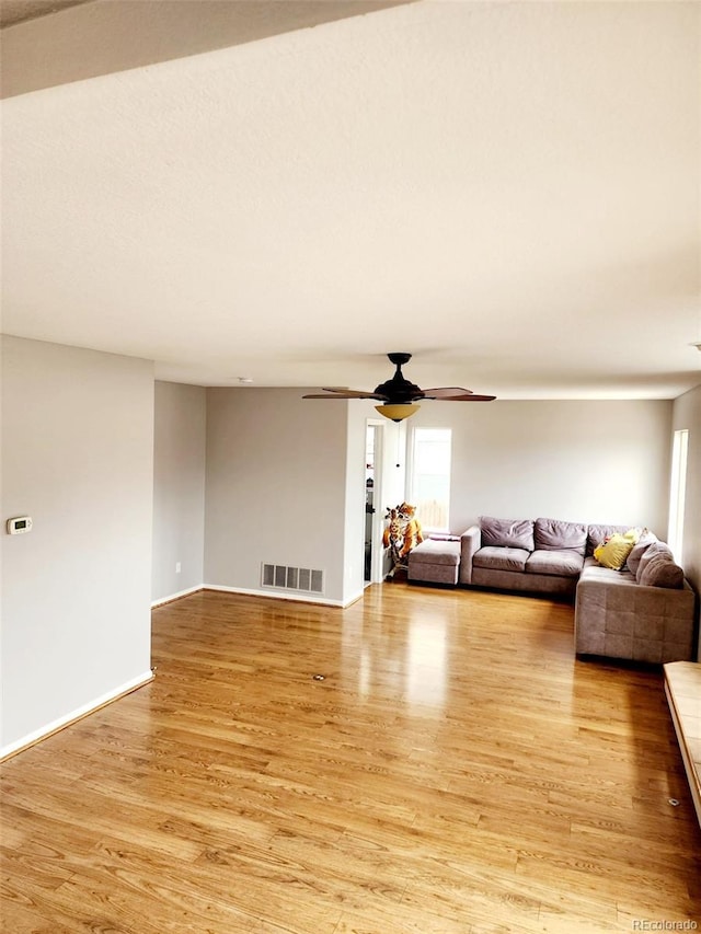 living room featuring light wood-style floors, visible vents, baseboards, and ceiling fan