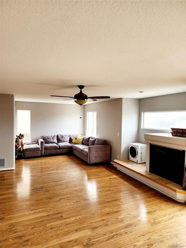 living room featuring a textured ceiling, wood finished floors, and a fireplace with raised hearth