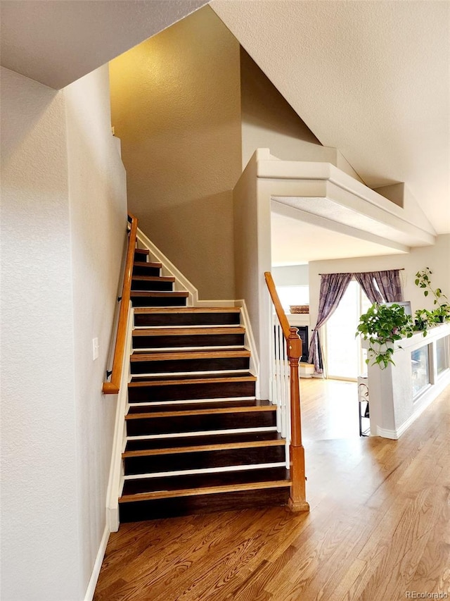 stairway with lofted ceiling, baseboards, and wood finished floors