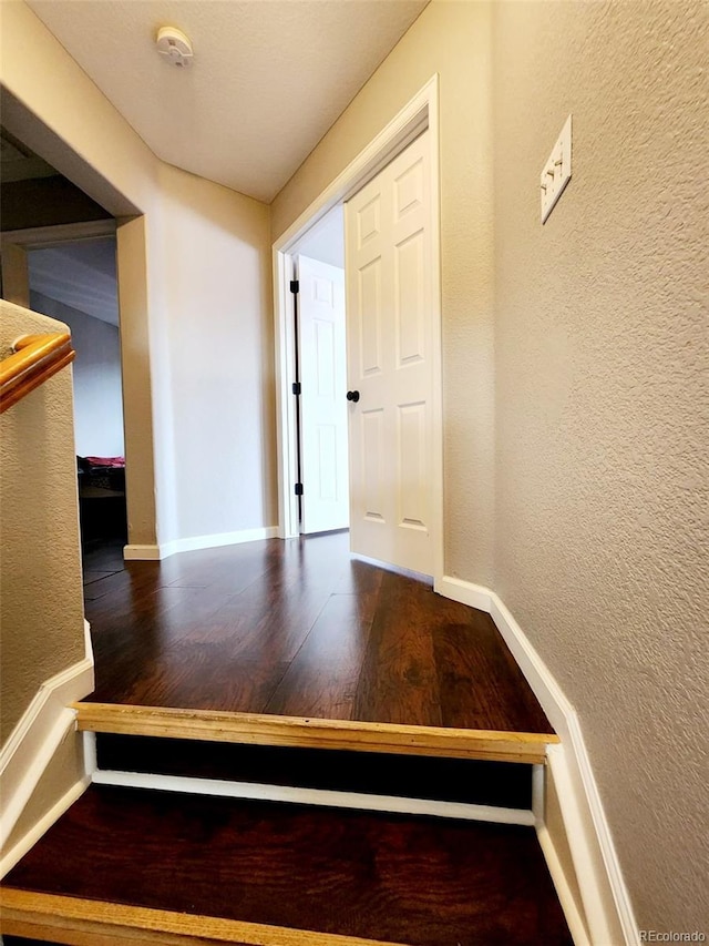 hall featuring wood finished floors, a textured wall, and baseboards