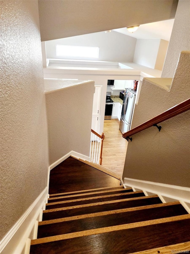 stairs with wood finished floors, a textured wall, and baseboards