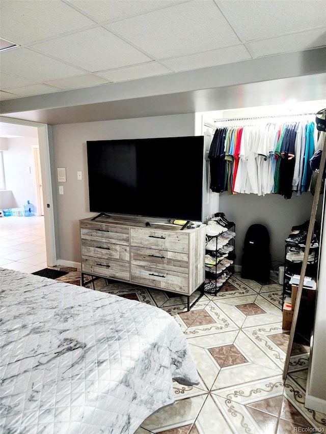 tiled bedroom featuring a drop ceiling and baseboards