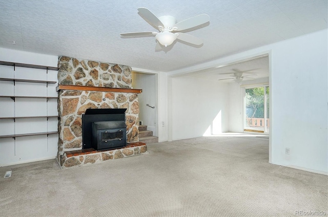 unfurnished living room with a fireplace, a wood stove, a textured ceiling, ceiling fan, and carpet