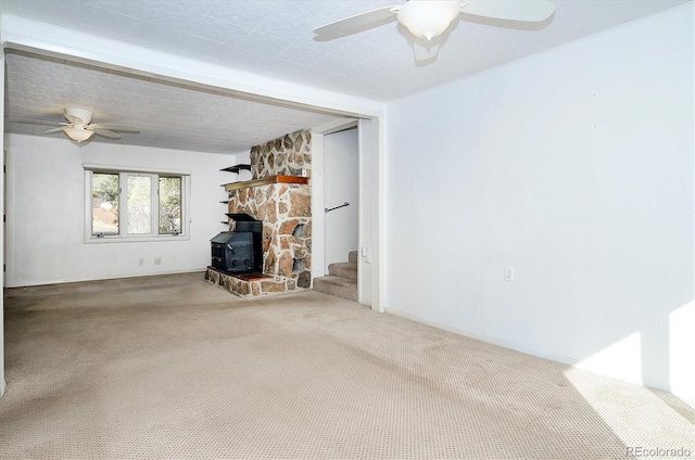 unfurnished living room with ceiling fan, a stone fireplace, a wood stove, and carpet