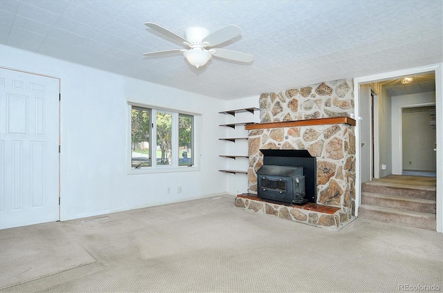 unfurnished living room with carpet floors, ceiling fan, and a wood stove