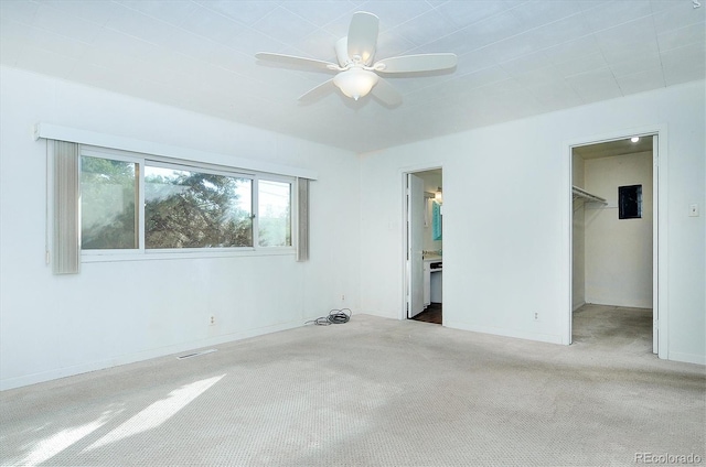 unfurnished bedroom with a closet, light carpet, ensuite bath, a walk in closet, and ceiling fan