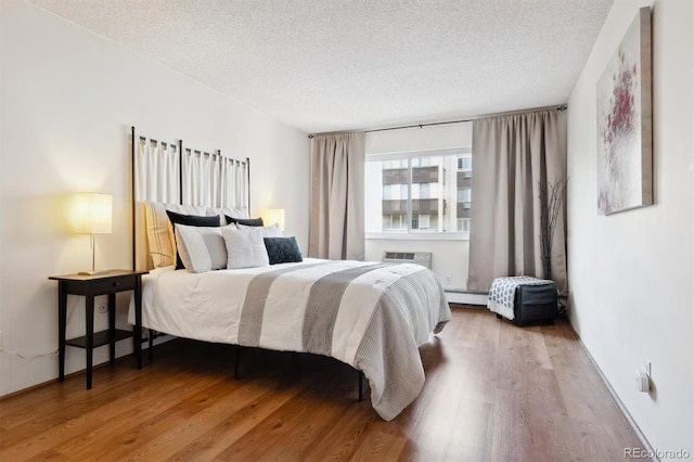 bedroom with wood-type flooring, an AC wall unit, a baseboard heating unit, and a textured ceiling