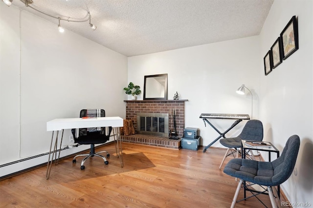 office area with a brick fireplace, wood-type flooring, rail lighting, and a textured ceiling