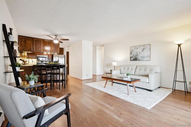 living room with ceiling fan, a textured ceiling, and light wood-type flooring