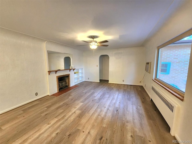 18 Columbia Dr, Julesburg, CO 80737 - unfurnished living room featuring radiator heating unit, arched walkways, a fireplace with flush hearth, wood finished floors, and a ceiling fan