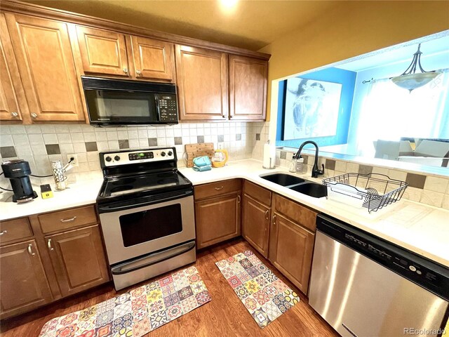 kitchen with light countertops, a sink, light wood-style flooring, tasteful backsplash, and appliances with stainless steel finishes