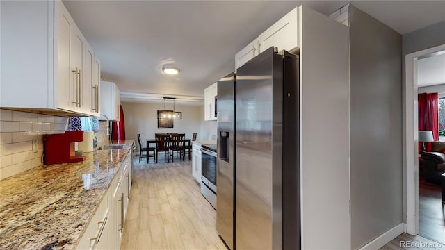 kitchen with pendant lighting, white cabinets, light wood-type flooring, appliances with stainless steel finishes, and light stone counters