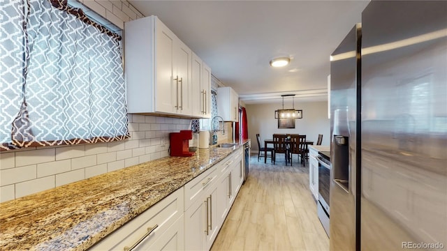 kitchen featuring light stone counters, light hardwood / wood-style floors, decorative backsplash, white cabinets, and appliances with stainless steel finishes