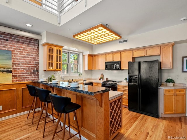 225 N Lincoln St Unit 4, Denver, CO 80203 - kitchen with black appliances, a peninsula, glass insert cabinets, light wood-style flooring, and a breakfast bar