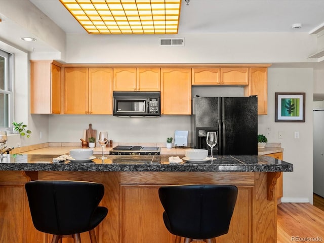 225 N Lincoln St Unit 4, Denver, CO 80203 - kitchen with black appliances, light brown cabinets, a kitchen bar, and light wood-style flooring