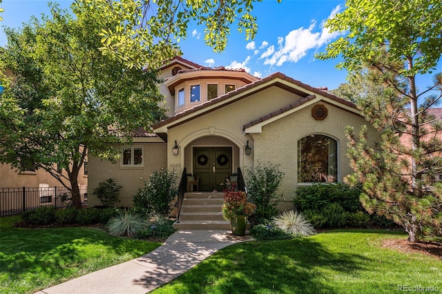 mediterranean / spanish-style home featuring a front lawn, a tiled roof, fence, and brick siding