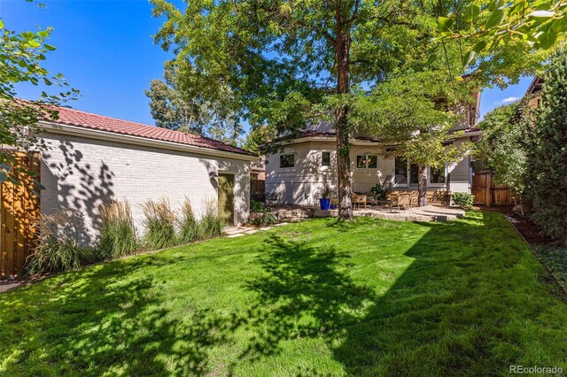 rear view of house with a patio, fence, a yard, a tile roof, and brick siding