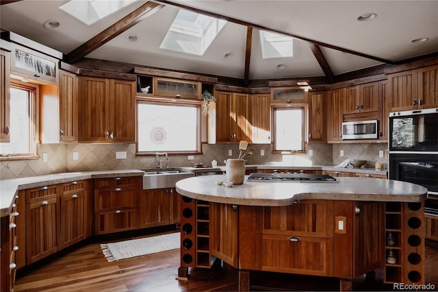 kitchen with a sink, open shelves, a kitchen island, vaulted ceiling with skylight, and appliances with stainless steel finishes