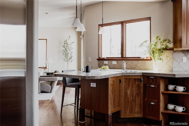 kitchen with tasteful backsplash, light countertops, a kitchen breakfast bar, dark wood-style floors, and a sink