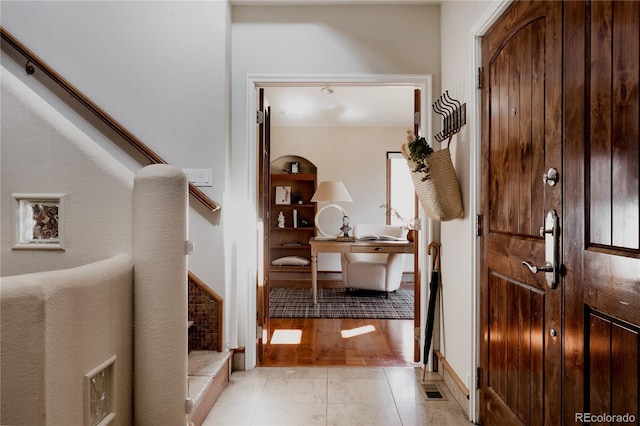 hall featuring light tile patterned floors, visible vents, and stairs