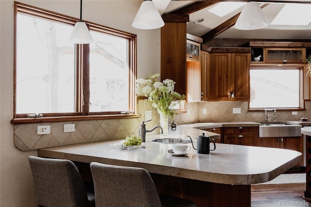 kitchen with decorative light fixtures, a peninsula, brown cabinetry, light countertops, and decorative backsplash