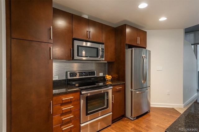 kitchen featuring stainless steel appliances, dark stone counters, light hardwood / wood-style floors, and decorative backsplash