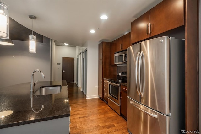 kitchen featuring sink, light hardwood / wood-style flooring, dark stone countertops, pendant lighting, and stainless steel appliances