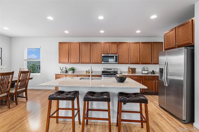 kitchen with appliances with stainless steel finishes, sink, a kitchen breakfast bar, light stone countertops, and a center island with sink