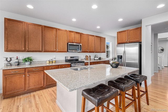 kitchen with sink, appliances with stainless steel finishes, a kitchen breakfast bar, light stone countertops, and an island with sink