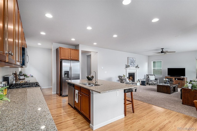 kitchen with a breakfast bar, sink, a center island with sink, appliances with stainless steel finishes, and light stone countertops