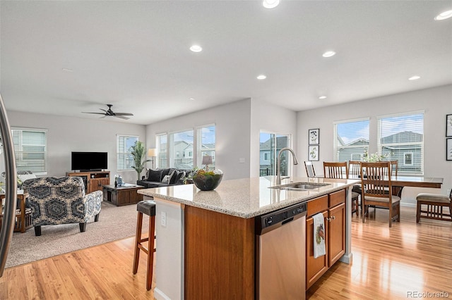 kitchen featuring sink, light hardwood / wood-style floors, light stone countertops, a center island with sink, and stainless steel dishwasher