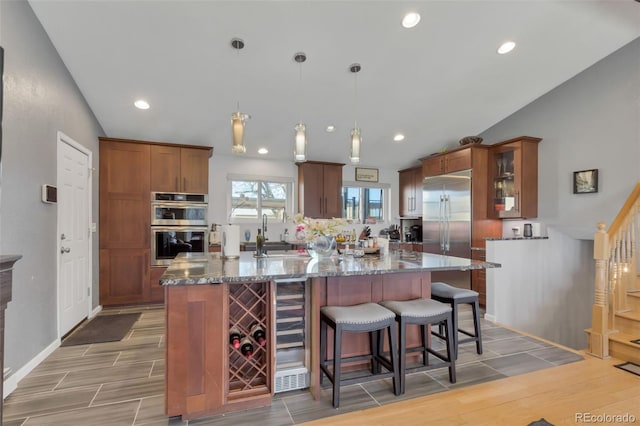 kitchen with sink, hanging light fixtures, vaulted ceiling, appliances with stainless steel finishes, and light hardwood / wood-style floors