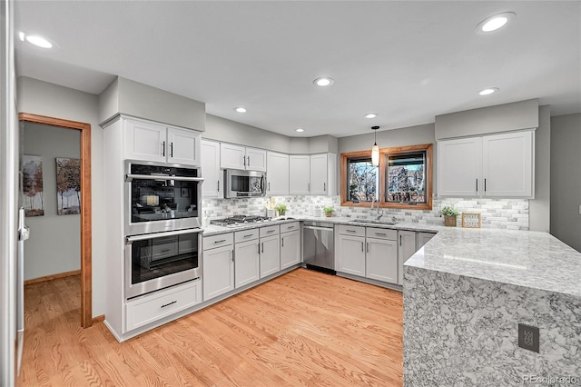 kitchen featuring sink, white cabinets, light hardwood / wood-style floors, stainless steel appliances, and light stone countertops