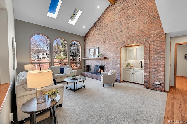 living room with sink, a skylight, high vaulted ceiling, light hardwood / wood-style flooring, and a fireplace