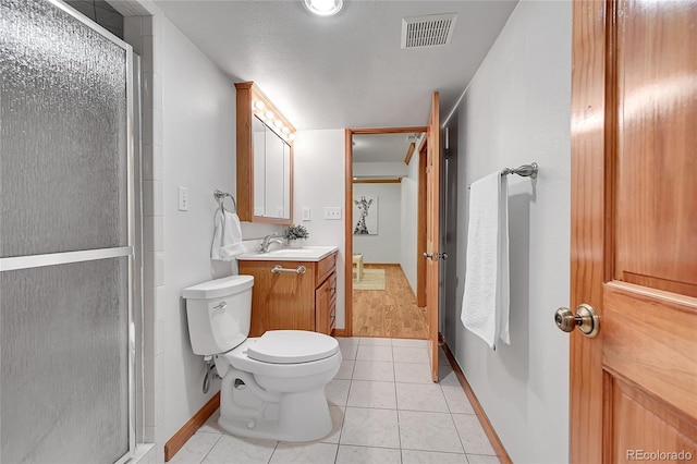 bathroom featuring tile patterned flooring, vanity, a shower with shower door, and toilet