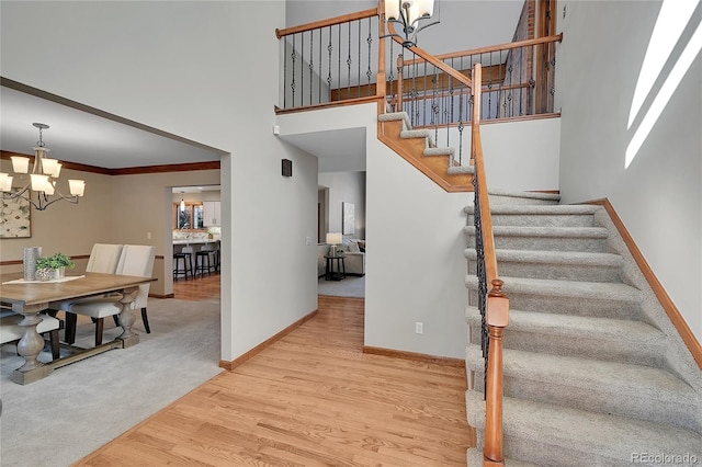 stairs featuring an inviting chandelier, crown molding, hardwood / wood-style floors, and a high ceiling