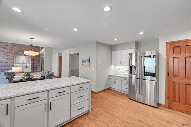 kitchen with brick wall, pendant lighting, white cabinets, stainless steel fridge, and light hardwood / wood-style flooring