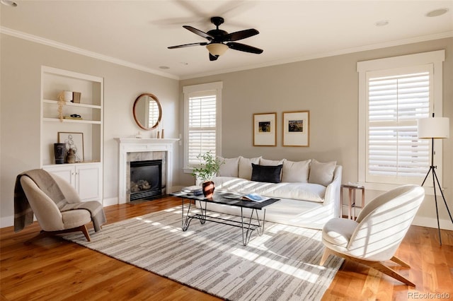 living room featuring a tiled fireplace, light wood-type flooring, built in shelves, and crown molding