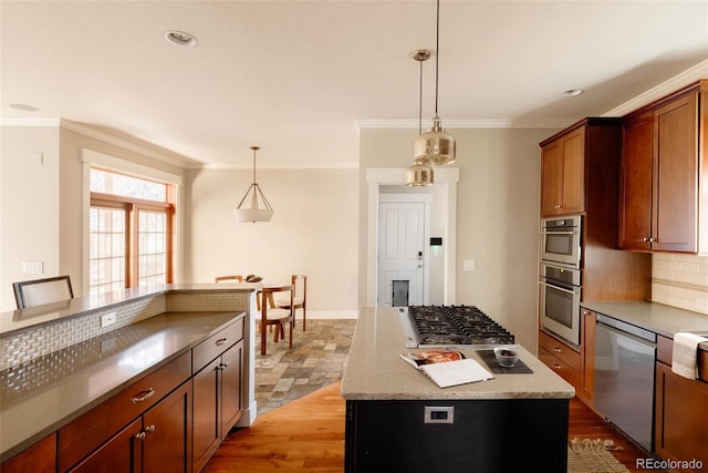 kitchen with stainless steel appliances, hanging light fixtures, ornamental molding, a kitchen island, and backsplash