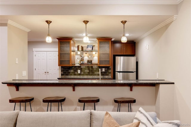 interior space featuring stainless steel fridge, backsplash, a breakfast bar area, and hanging light fixtures